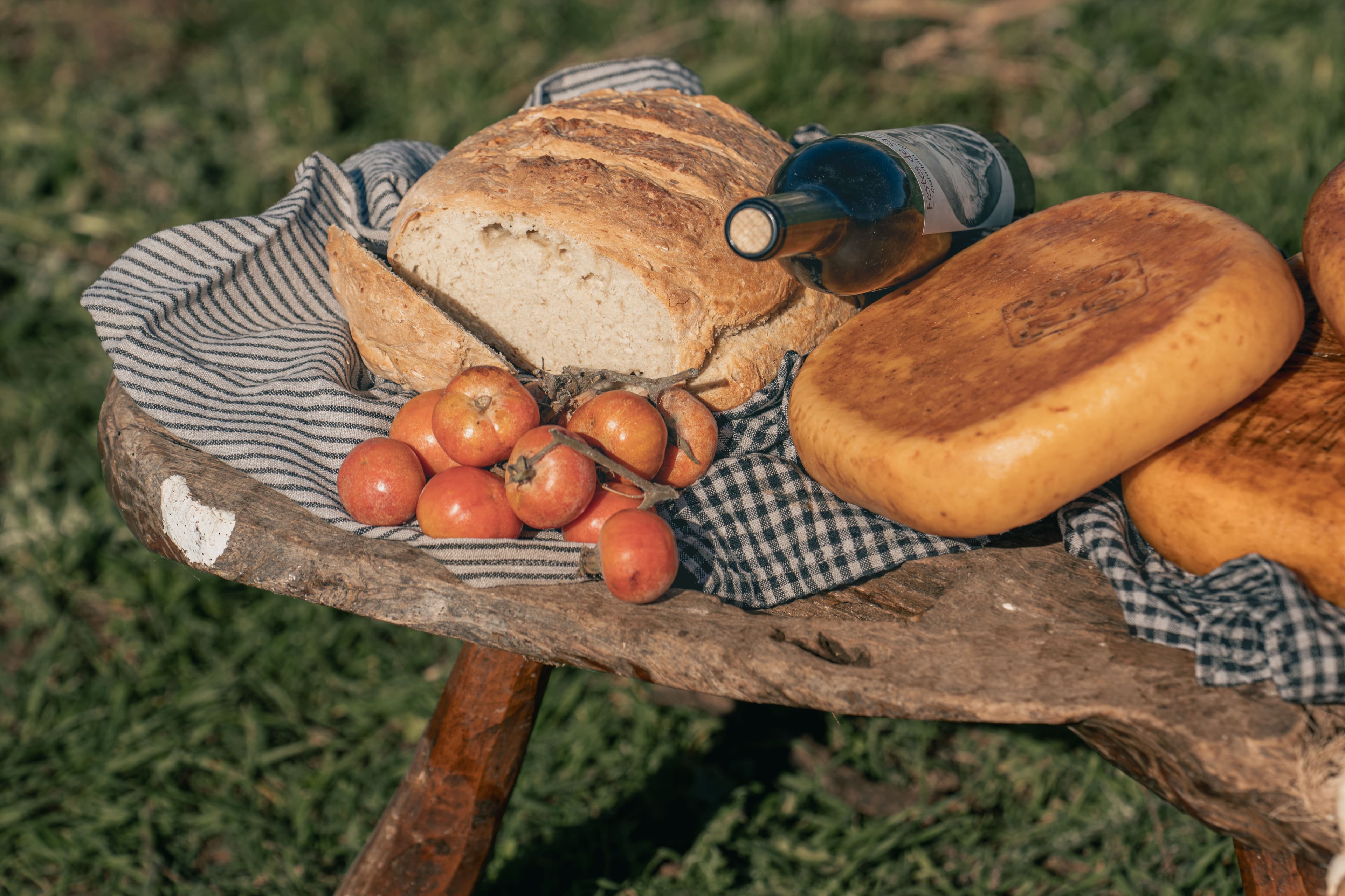 Queso artesano, pan, tomates y una botella sobre una mesa rústica